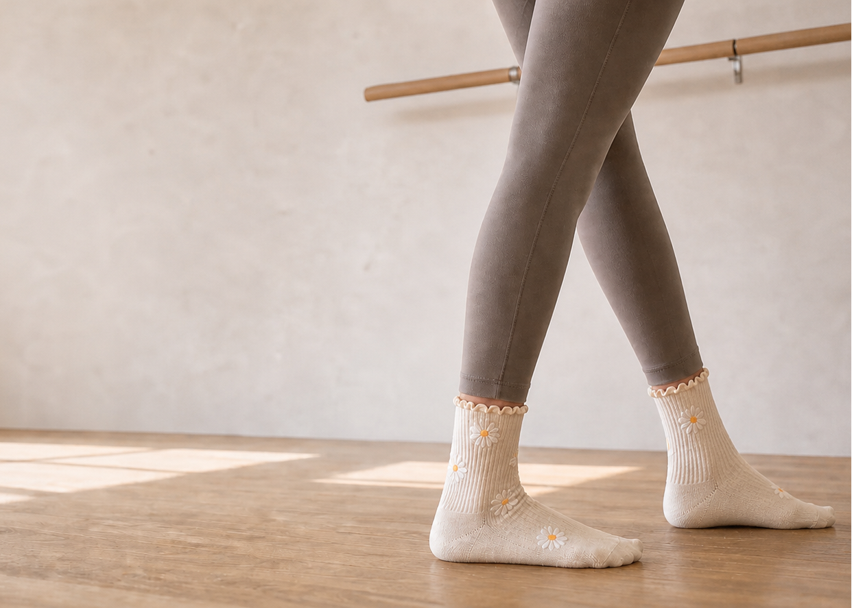 Person wearing gray leggings and white socks standing in a dance studio with a ballet barre.