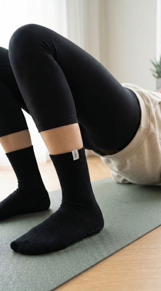 Person wearing black korr grip socks and leggings on a yoga mat in a home setting